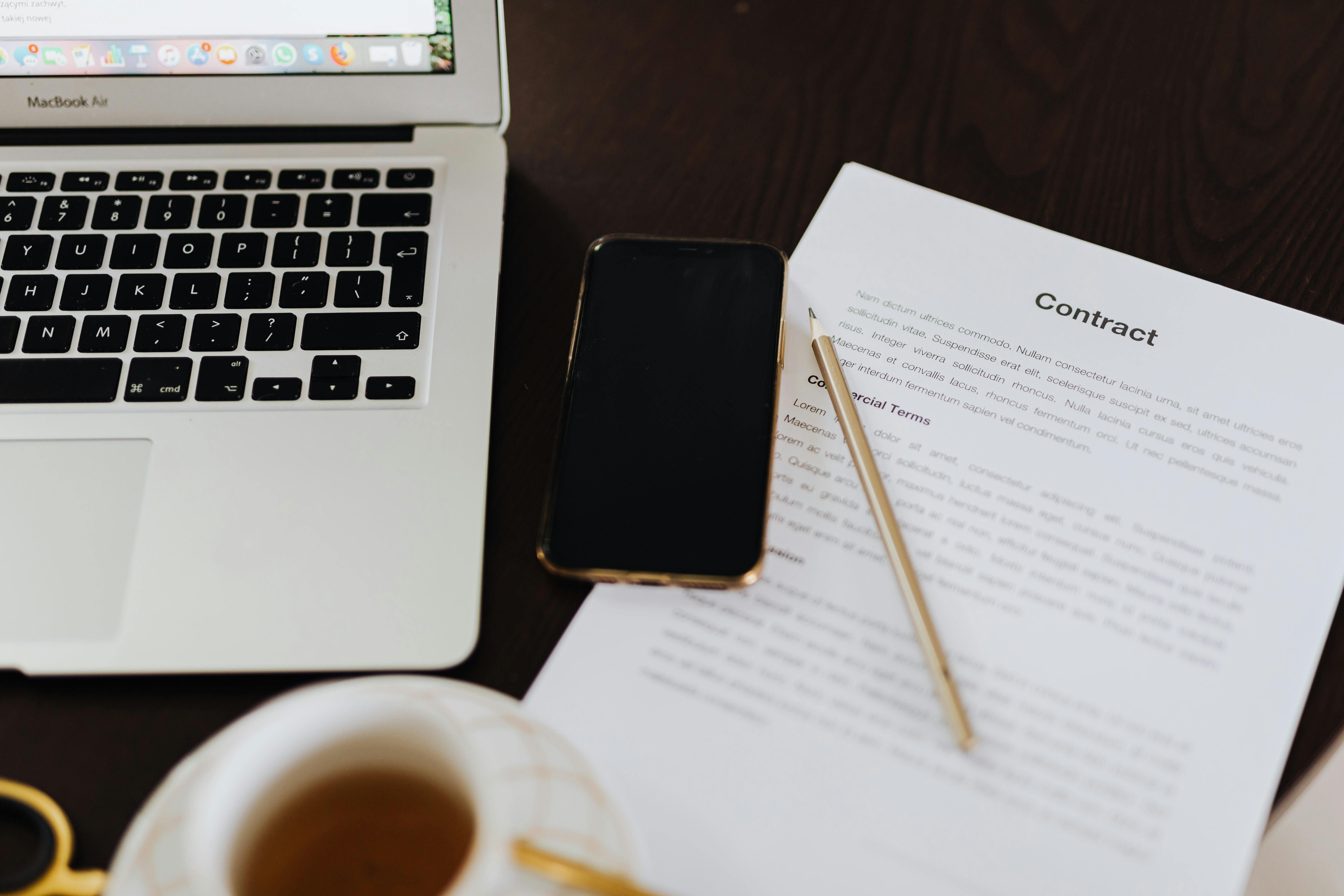Contract document, laptop, smartphone, and pen arranged on a desk for portfolio review.